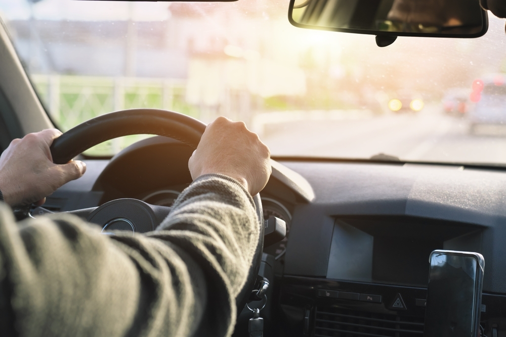 Men’s driver's hand holding steering wheel of car while driving. Transportation and travel scene.