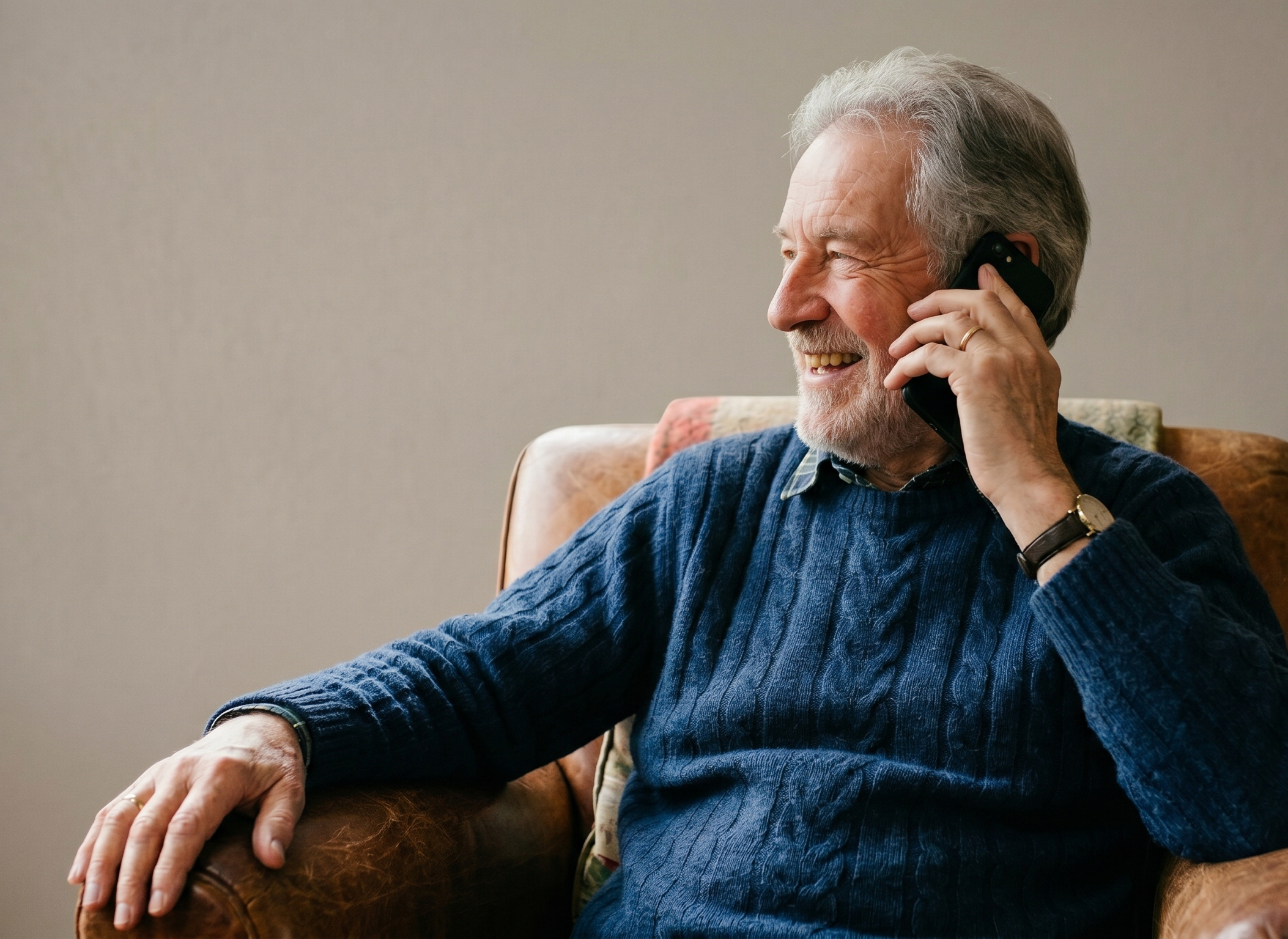 elderly man laughin in a chair whilst on the phone