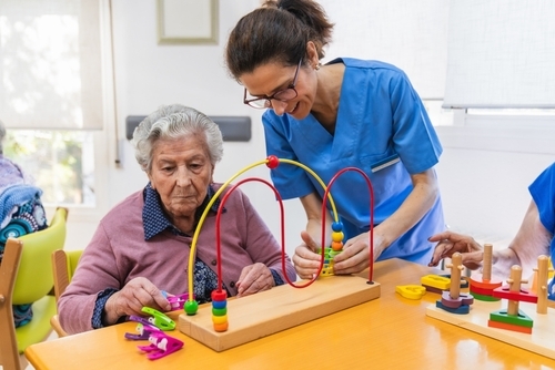 Nurse helps an elderly woman with a cognitive therapy toy in a nursing home, focusing on mental engagement and physical coordination