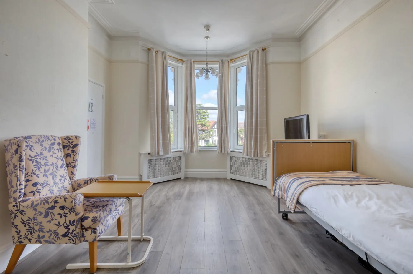 Spacious room with large bay window and a single bed with one chair in the room