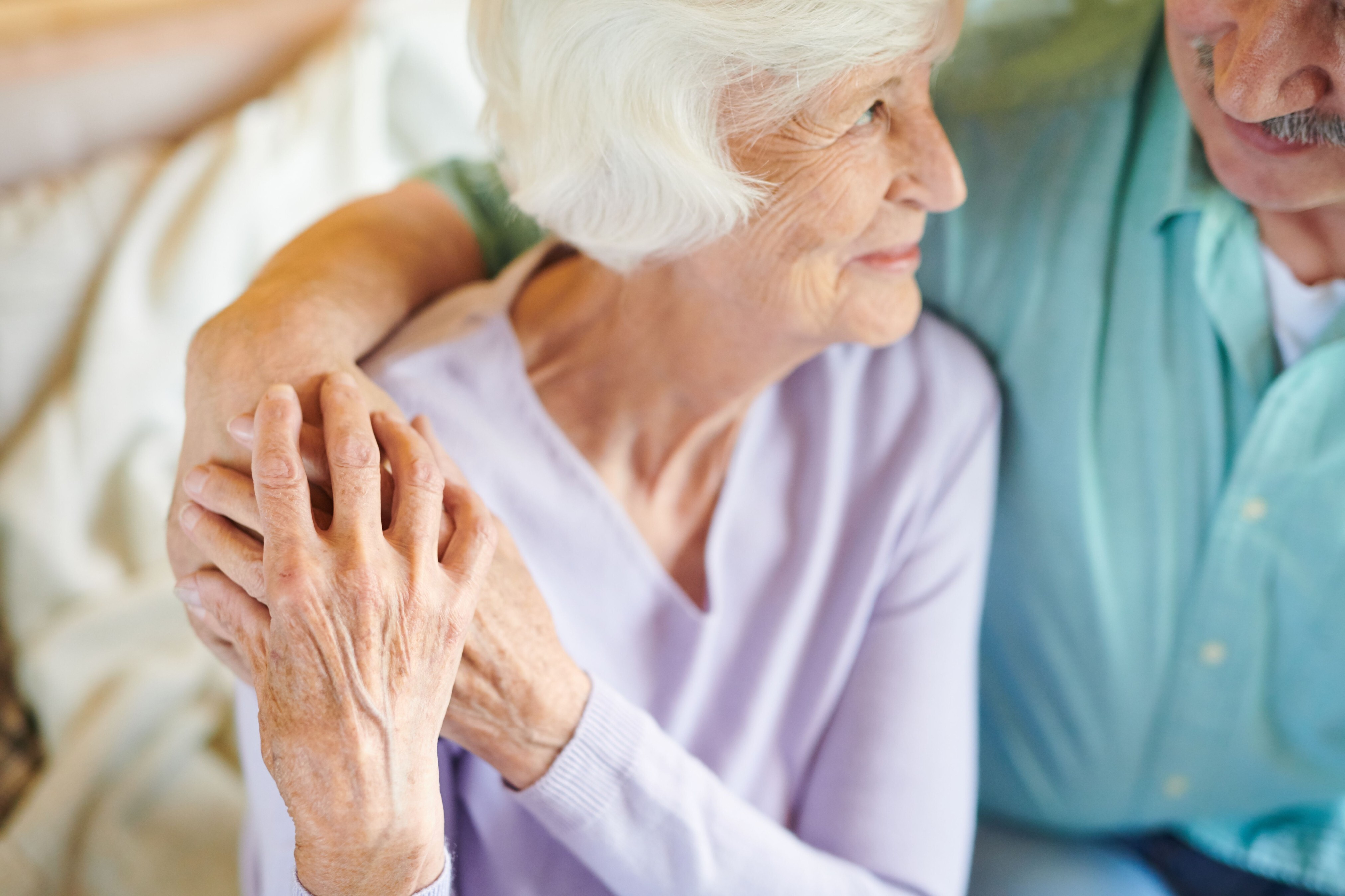 An elderly couple with the man having an arm around the lady and her hands on top of his, looking lovingly into each other's eyes.